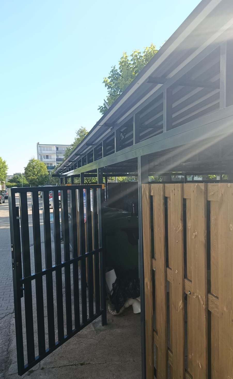 Wiata śmietnikowa - otwarta furtka z widokiem na pojemniki na odpady